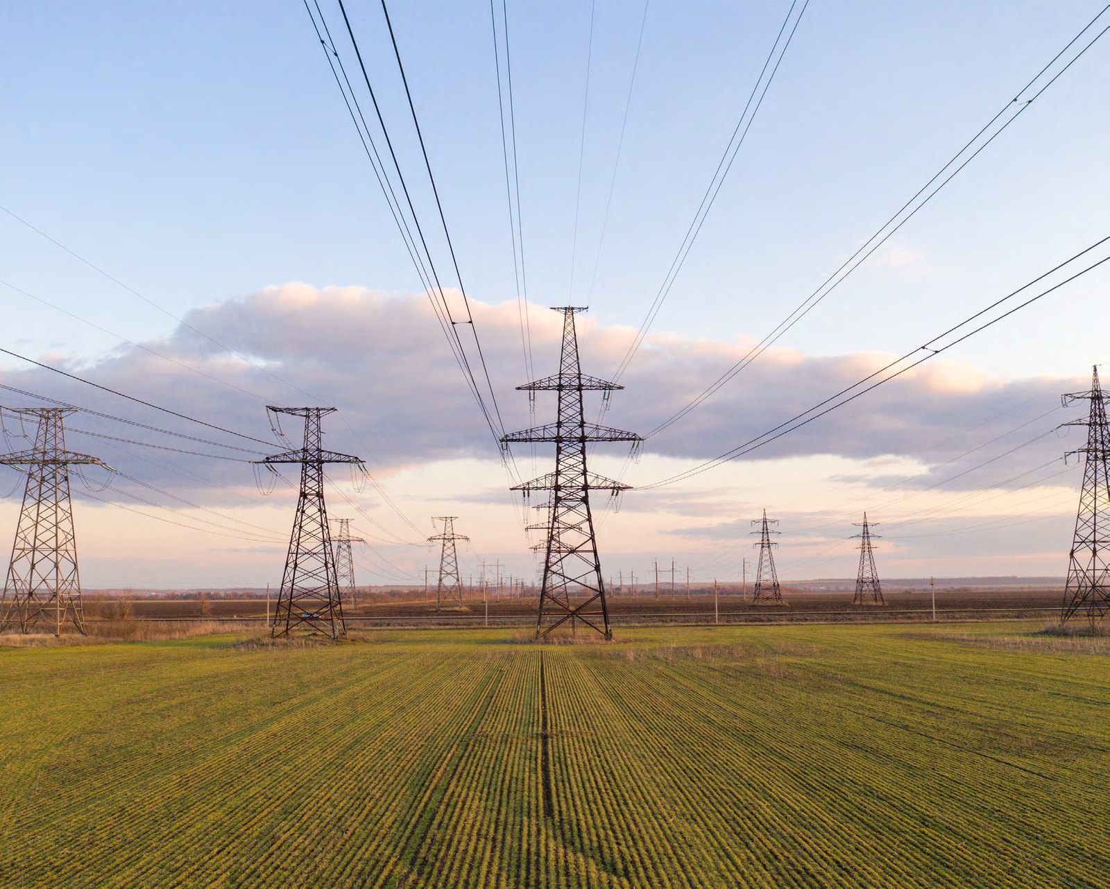 High-voltage transmission towers crossing an open field at dusk